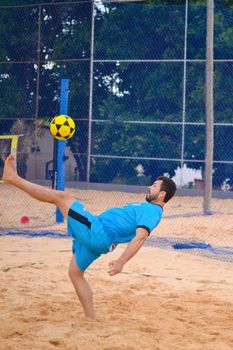 Athletic man executing a bicycle kick on a sandy beach soccer court.