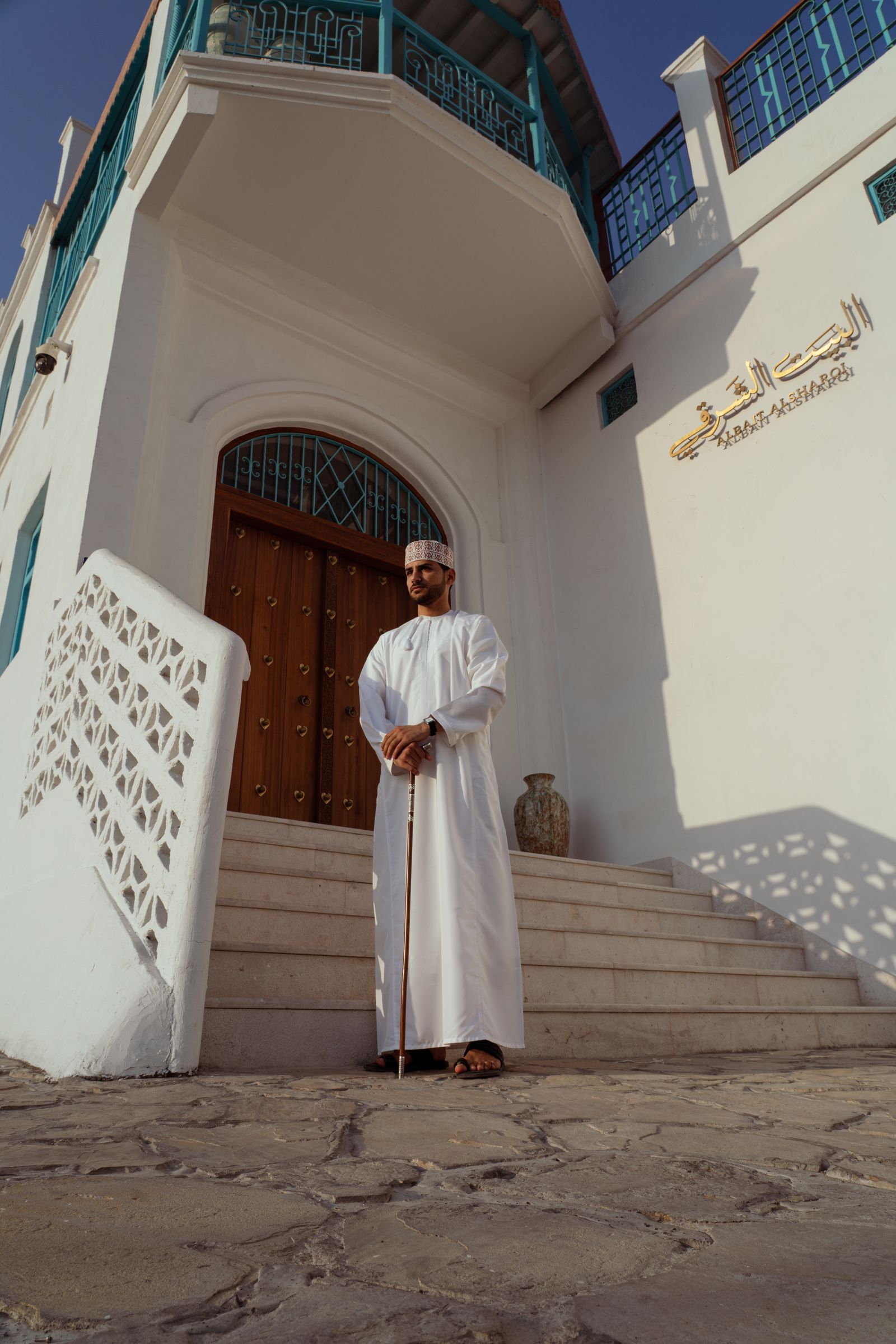 A man wearing a white dishdasha and patterned Omani cap on steps outside a building in Muscat, Oman