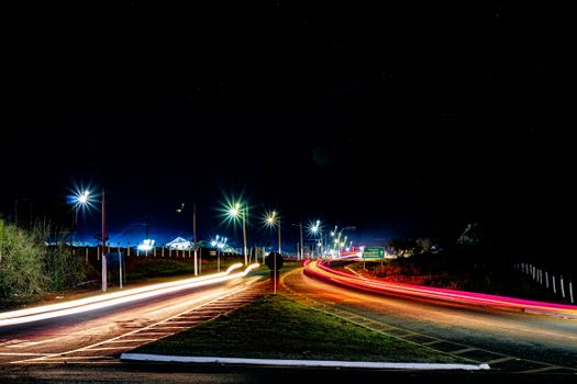 A stunning capture of car light trails on a winding road at night under a starry sky.