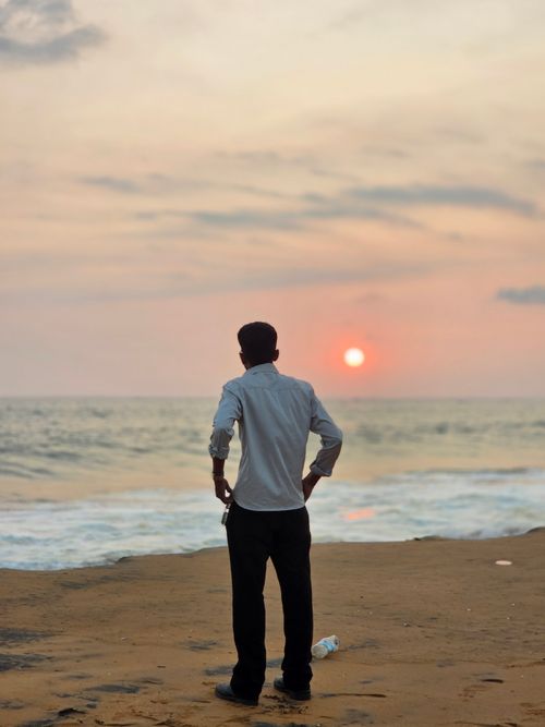 Free A person stands on the beach watching a serene sunset over the ocean waves. Stock Photo