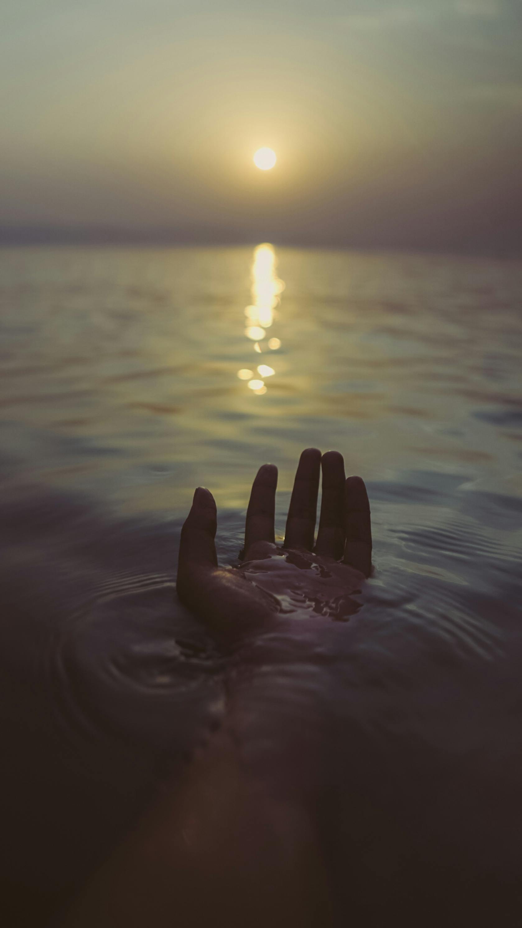 gratis Een silhouet van een hand die door het kalme water reikt tijdens een serene zonsondergang. Stockfoto