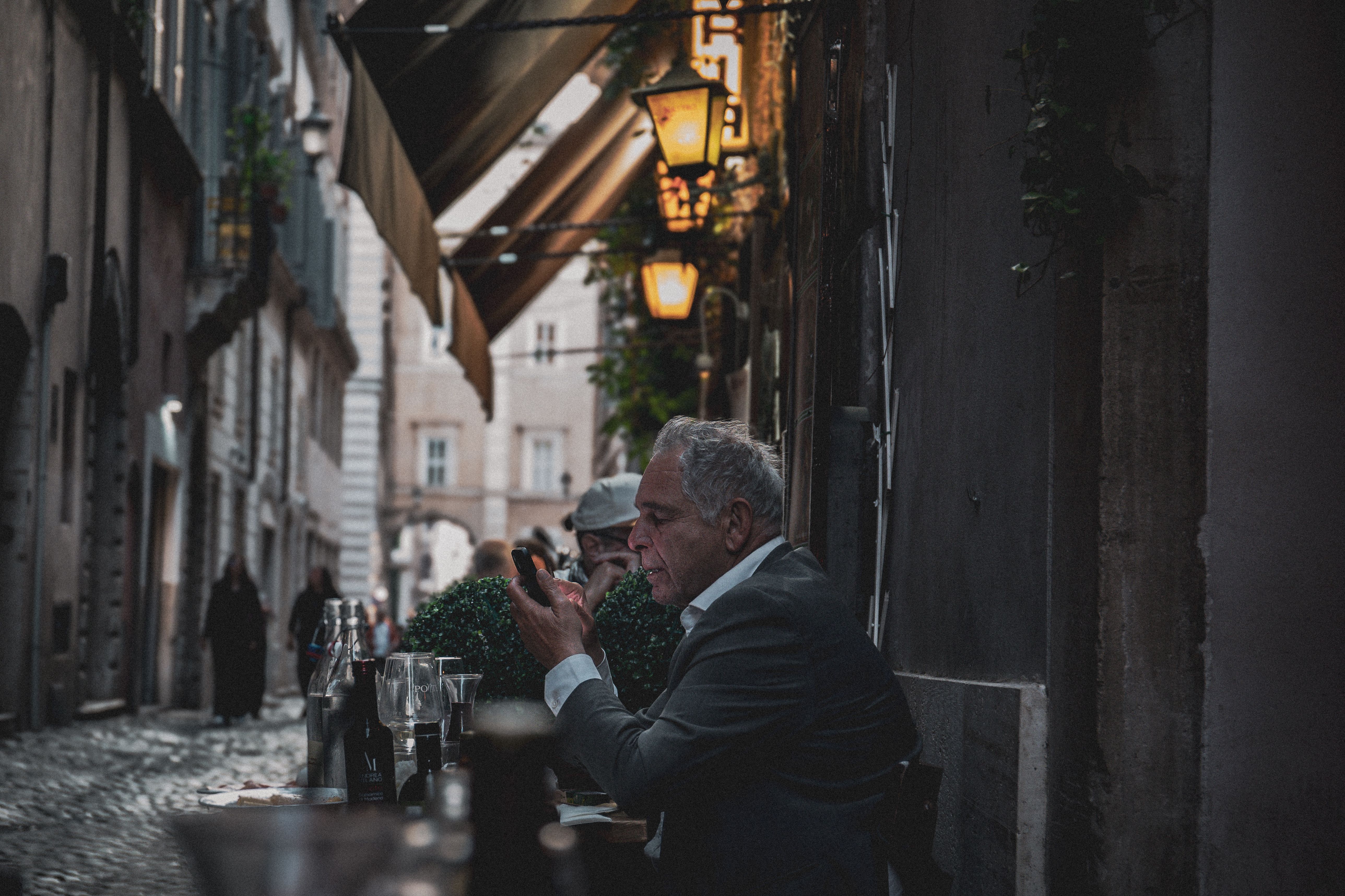 A moody evening street scene in Rome, Italy, capturing relaxed dining under warm lamplights.