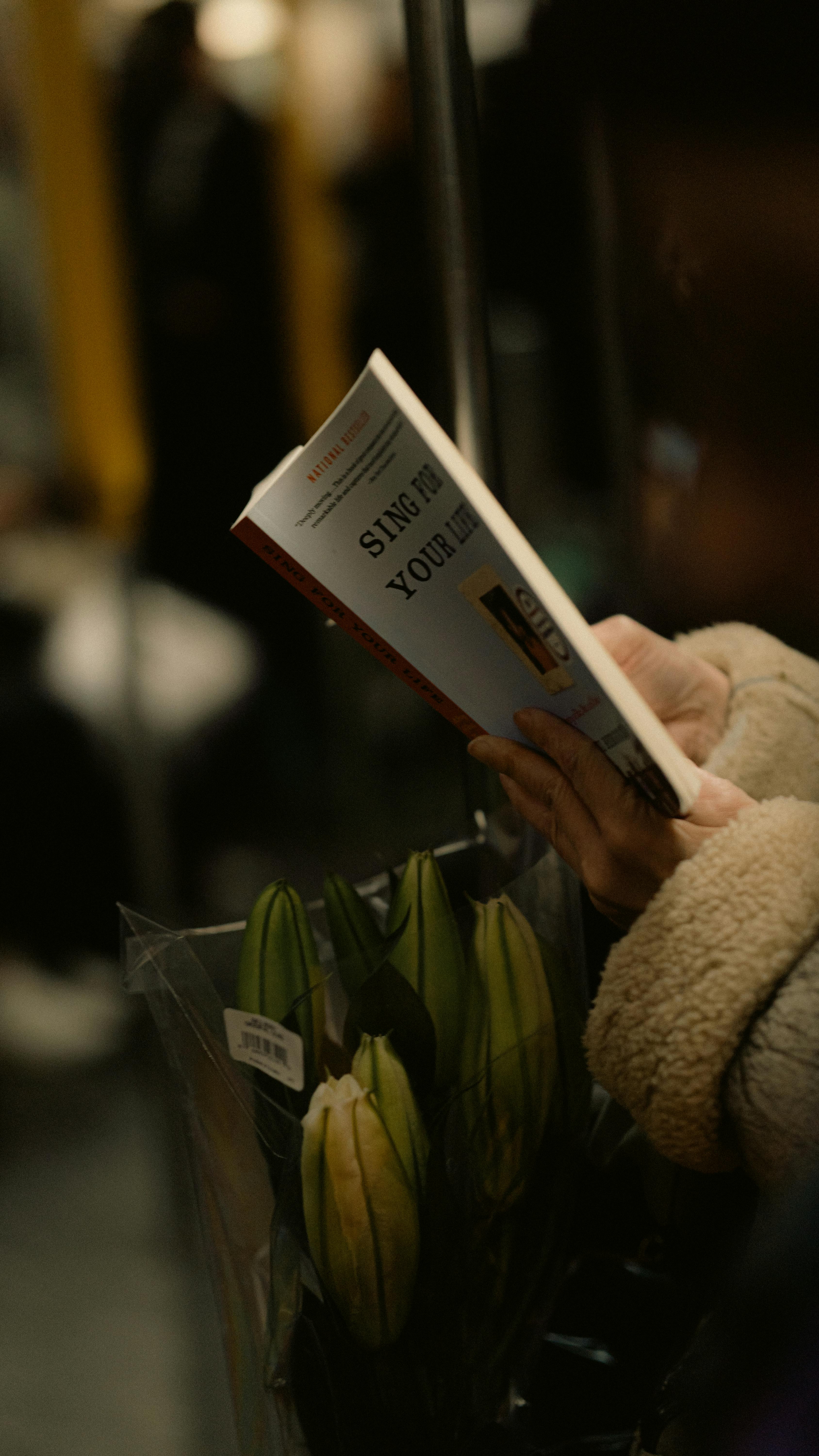 Miễn phí Một người đang đọc sách trên tàu điện ngầm New York, tay cầm một bó hoa, khoảnh khắc thân mật. Ảnh lưu trữ