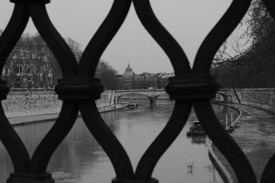 Artistic view of the Tiber River through a wrought iron fence in Rome.