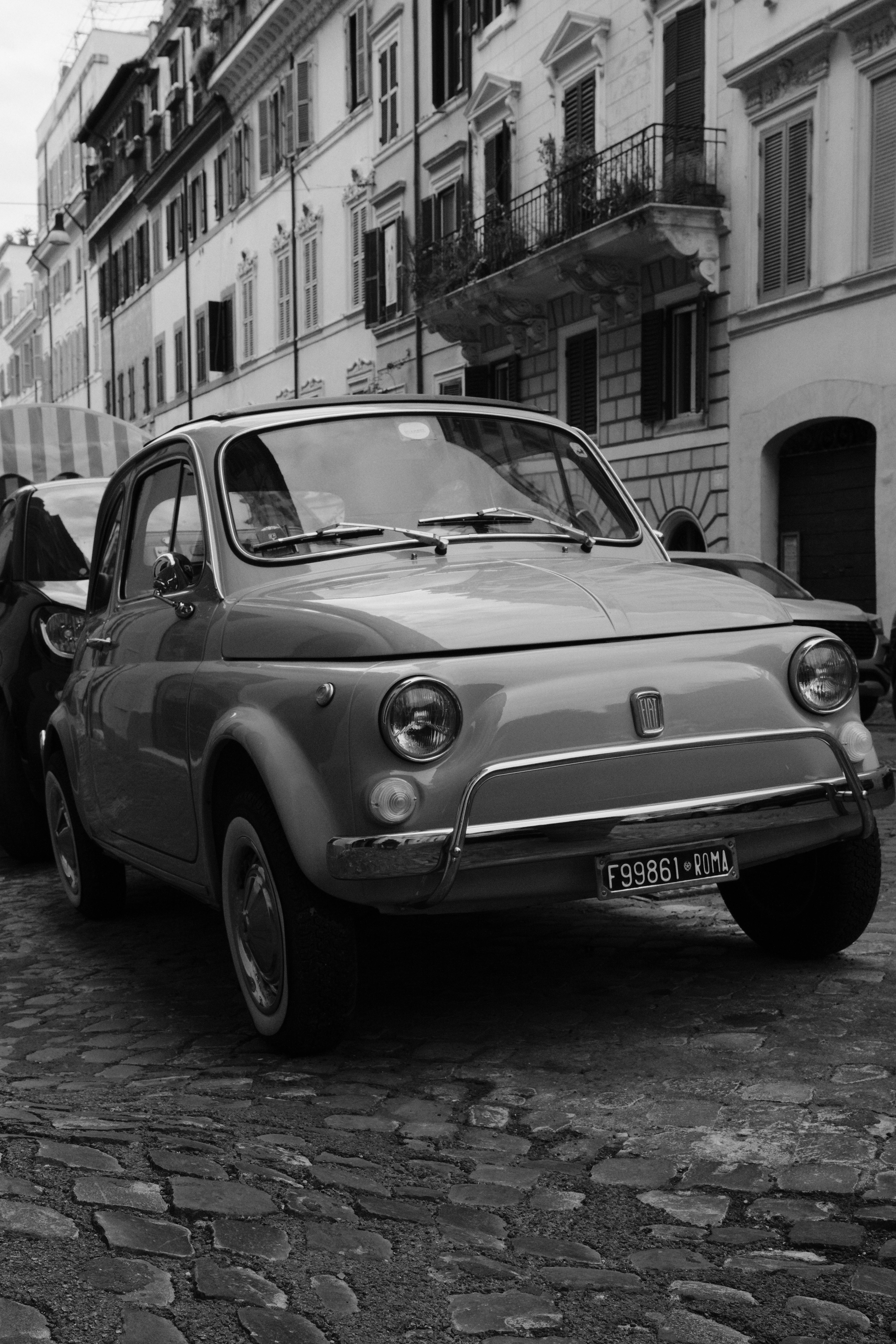 Miễn phí Chiếc Fiat 500 cổ điển đậu trên con phố lát đá cuội ở Rome, Ý. Hình ảnh đen trắng làm nổi bật vẻ đẹp cổ kính. Ảnh lưu trữ