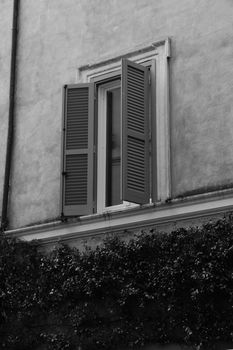 Black and white photo of an open window with shutters in Rome, Italy, showcasing classic architecture.