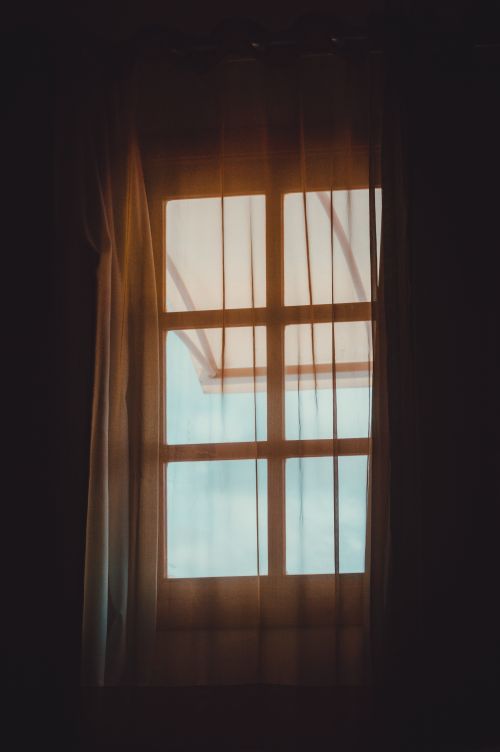 Free Cozy interior view through sheer curtains and a bright window, casting warm light indoors. Stock Photo