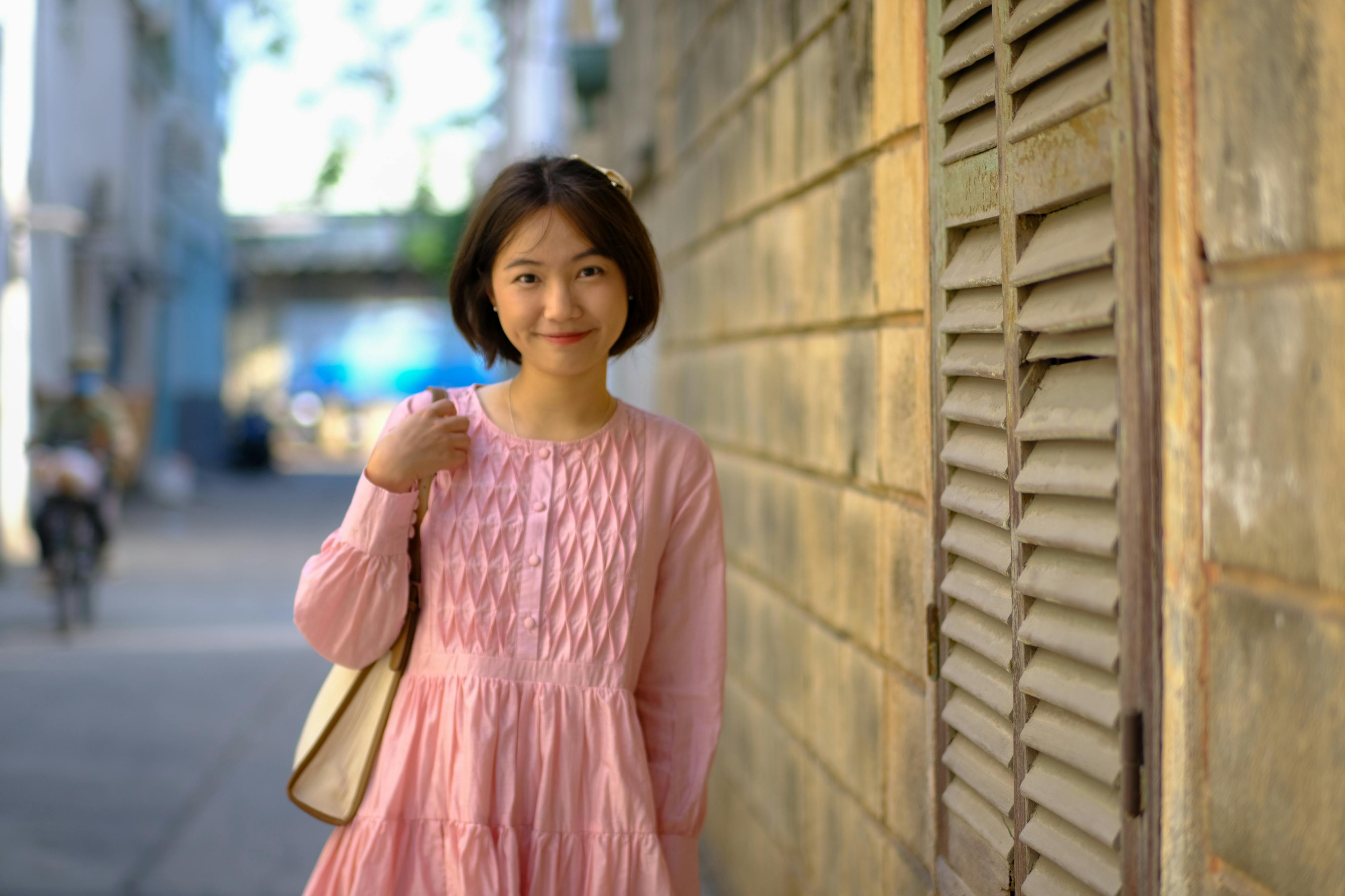 Безкоштовне Весела молода жінка в рожевій сукні посміхається у провулку в Хошиміні. стокове фото