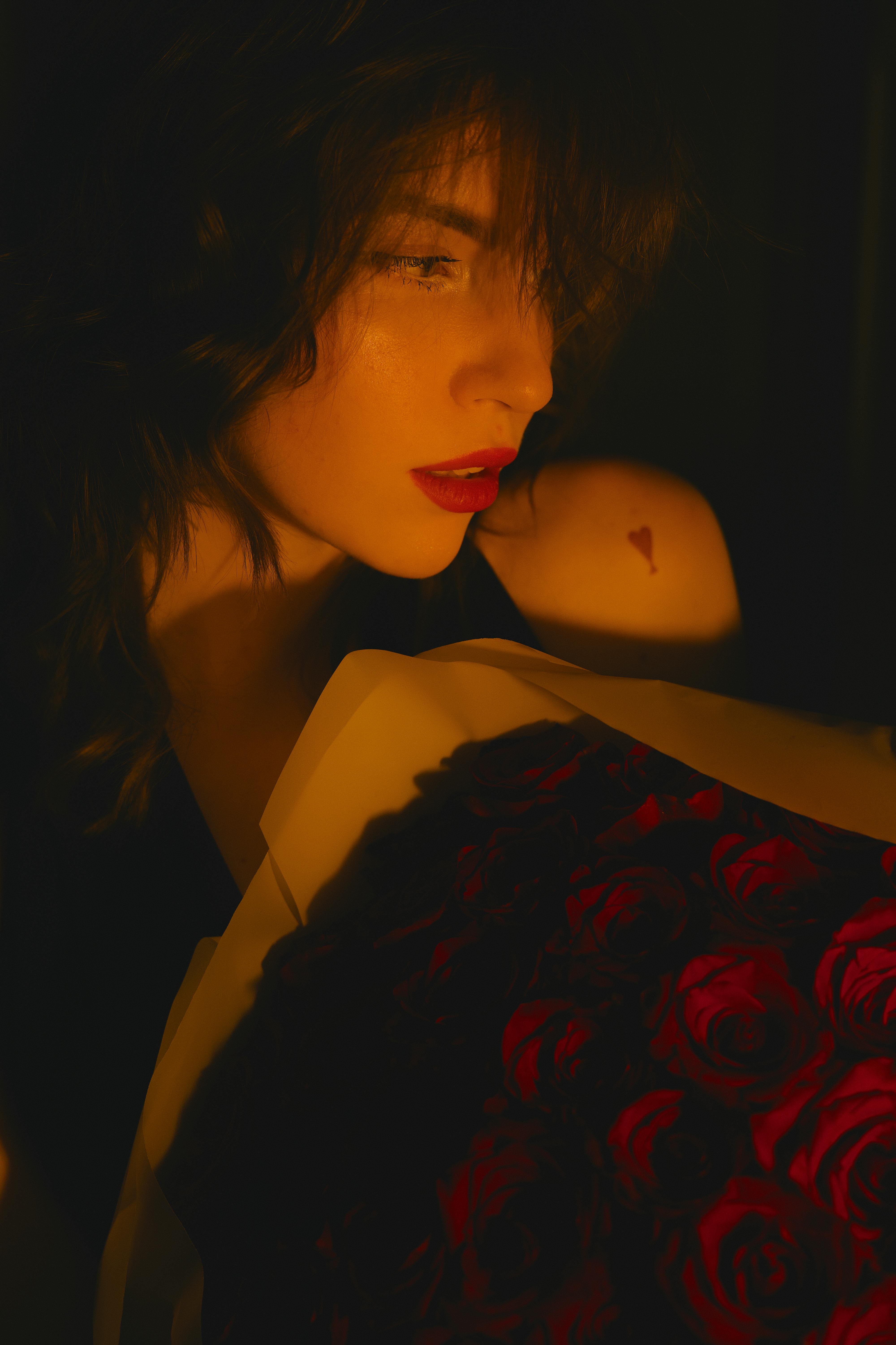 Miễn phí Bức chân dung đầy cảm xúc của một người phụ nữ với những bông hồng đỏ và hình xăm trên cánh tay, dưới ánh sáng dịu nhẹ. Ảnh lưu trữ