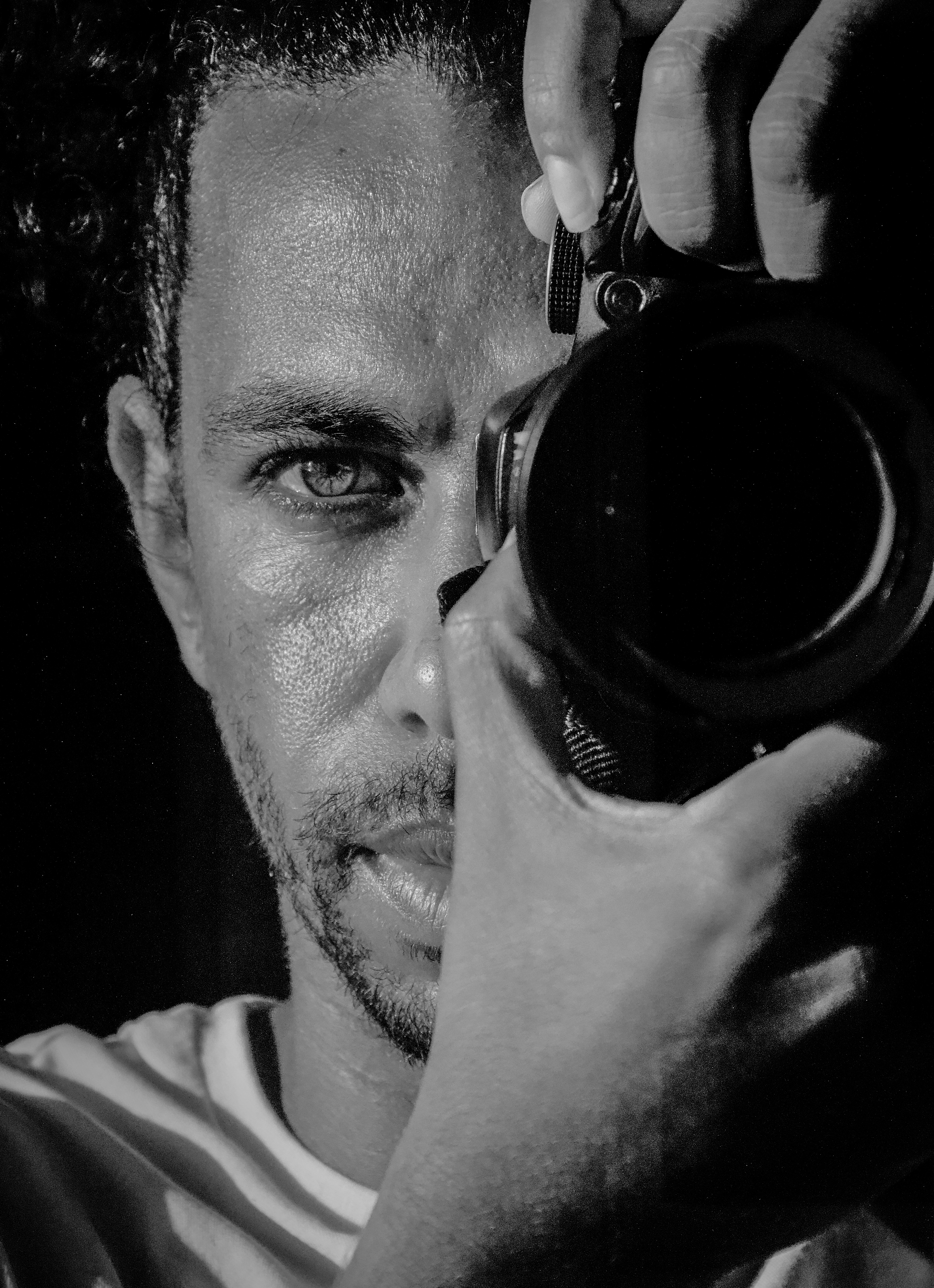Intense black and white portrait of a male photographer holding a camera, focused on the lens.