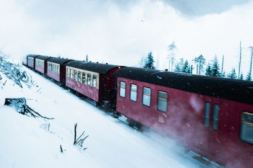 Free A red train travels swiftly through a snowy winter landscape, surrounded by frosted trees and snowflakes. Stock Photo