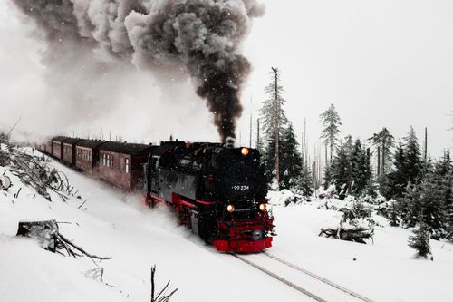 Free A vintage steam train travels through a snow-covered forest, emitting thick smoke under a winter sky. Stock Photo