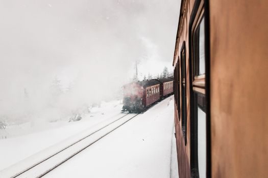 A steam train travels through a snow-covered forest, enveloped in mist and cold winter atmosphere.
