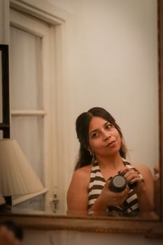 A woman in striped attire captures a self-portrait in a mirror indoors.