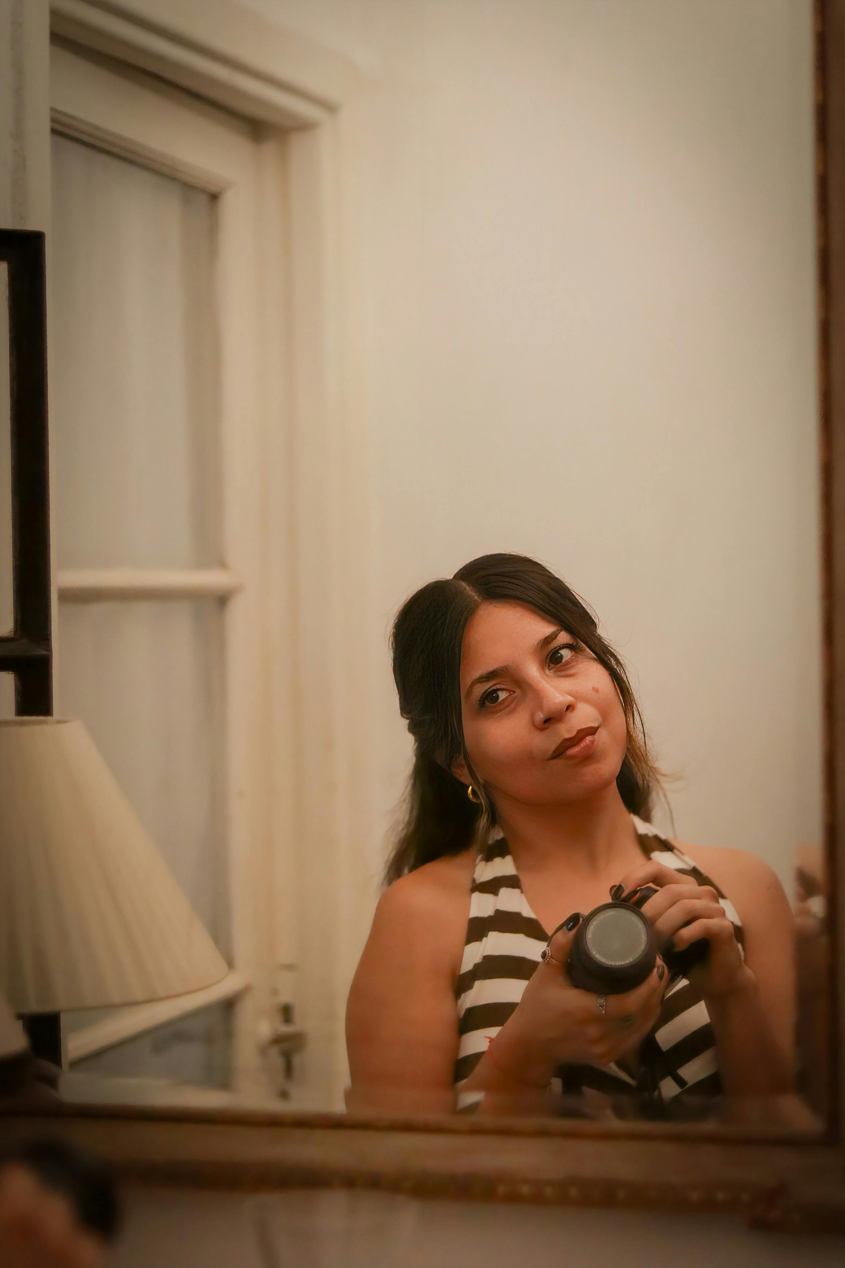 ingyenes Egy csíkos ruhás nő önarcképet készít egy tükörben zárt térben. Stockfotó