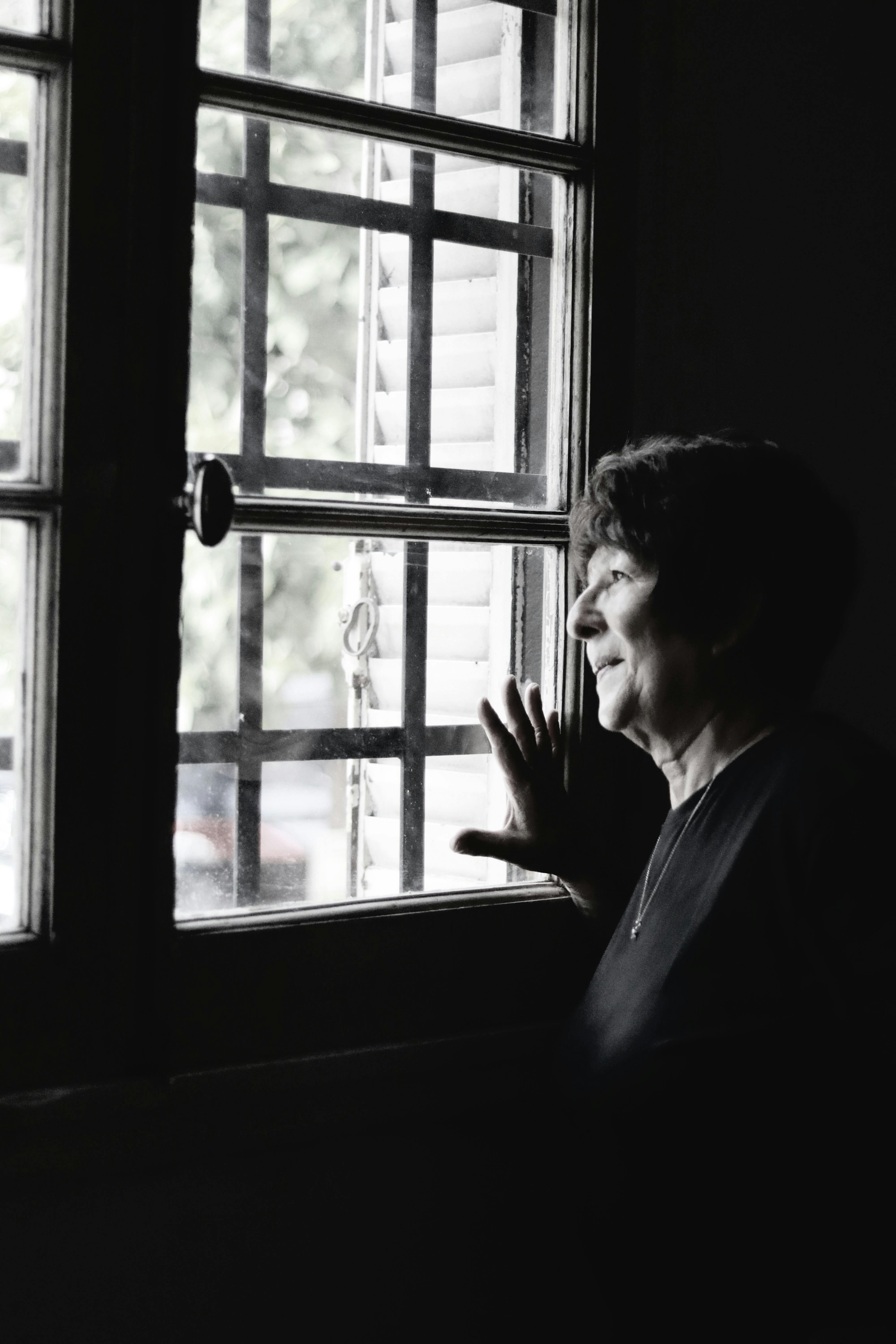 무료 한 노년 여성이 창밖을 사색에 잠긴 듯 바라보며 실내로 들어오는 자연광을 만끽하고 있다. 스톡 사진