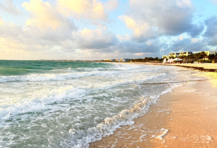 A serene Caribbean beach scene with gentle waves and a vibrant sunrise sky.
