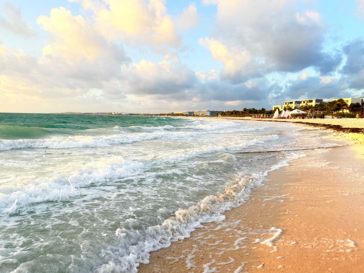 A serene Caribbean beach scene with gentle waves and a vibrant sunrise sky.