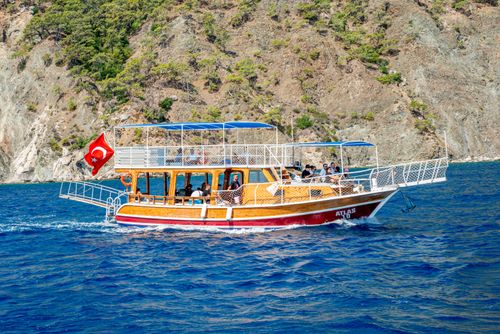 Free A Turkish boat with flag sailing near a rocky coastline on a clear summer day. Stock Photo