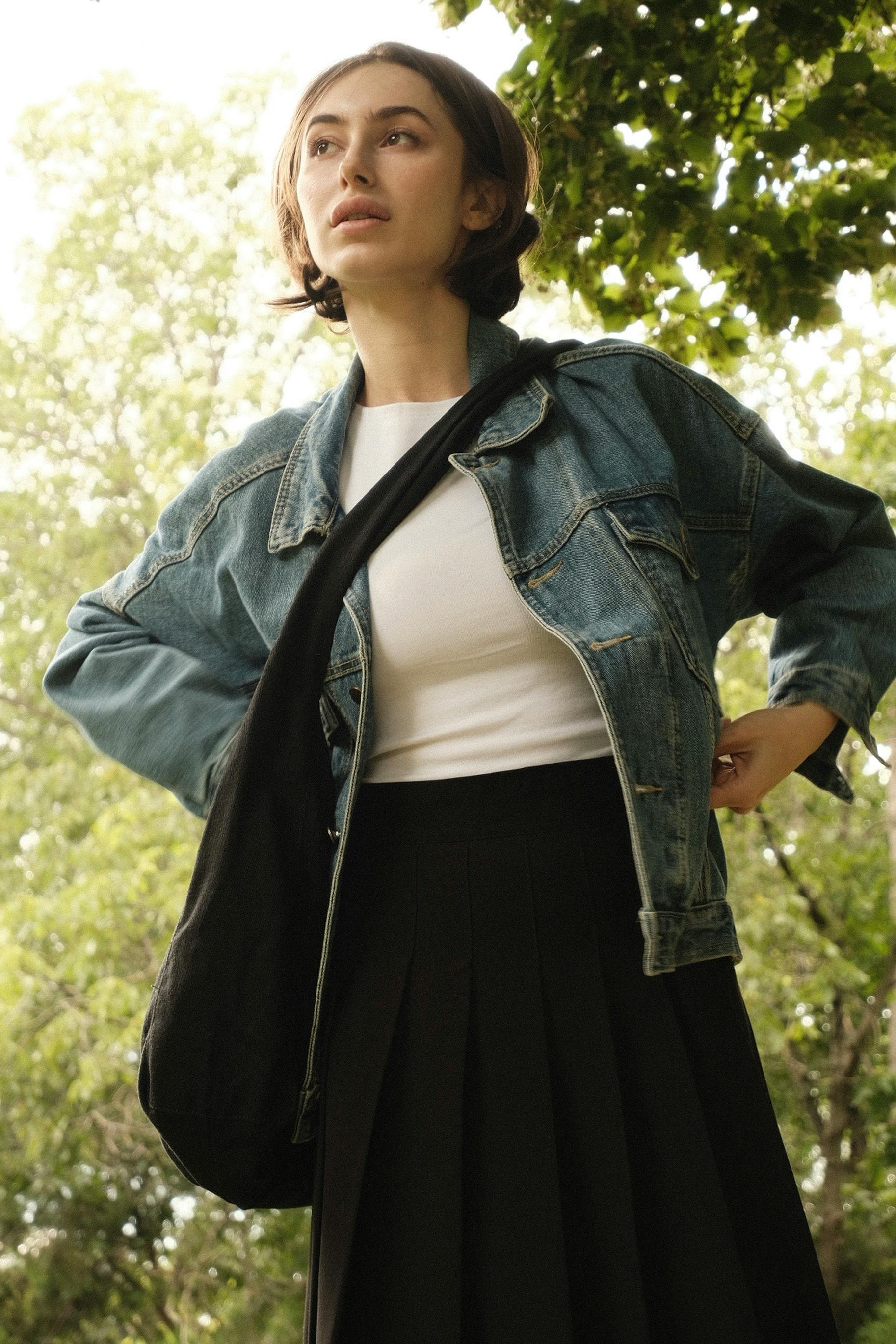 무료 데님 재킷을 입은 젊은 여성이 공원을 배경으로 서 있는 모습의 초상화. 스톡 사진