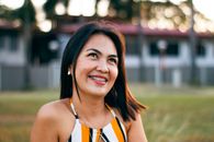 Delighted young Asian lady smiling while chilling on grassy meadow during summer holidays