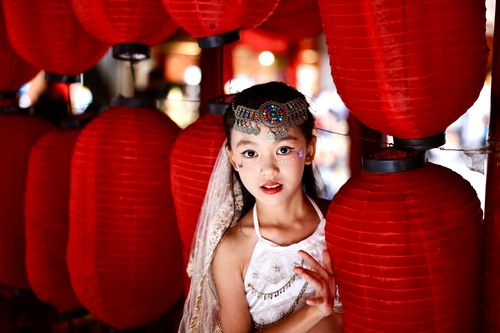 Free A young girl in festive attire stands among vibrant red lanterns, evoking a celebratory and cultural atmosphere. Stock Photo