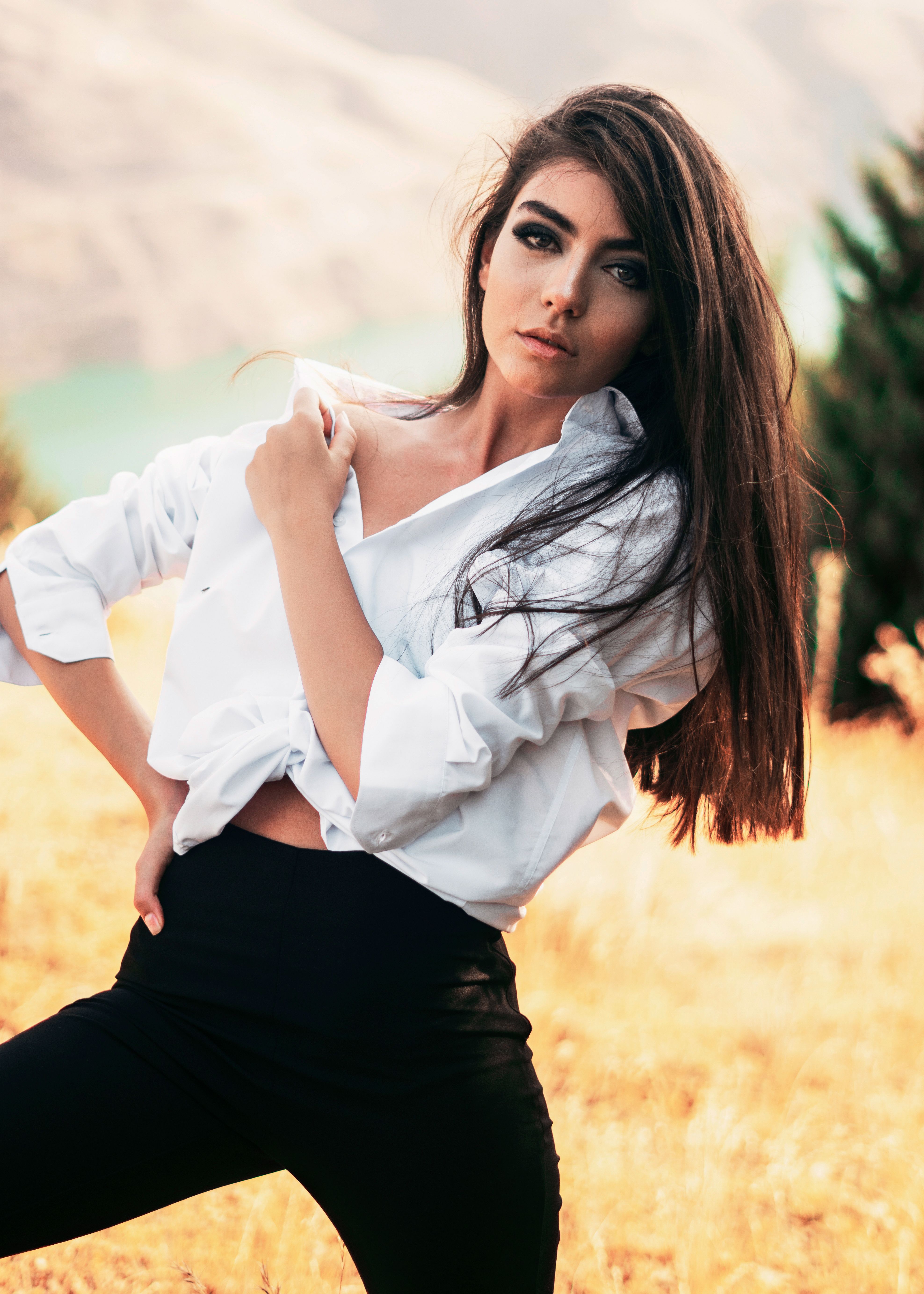 Portrait of a fashionable woman posing confidently outdoors with long hair and a white shirt.