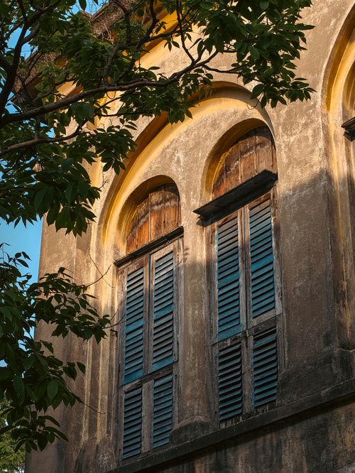 Free Charming view of a historic colonial building facade in Kolkata, India with sunlight filtering through leaves. Stock Photo