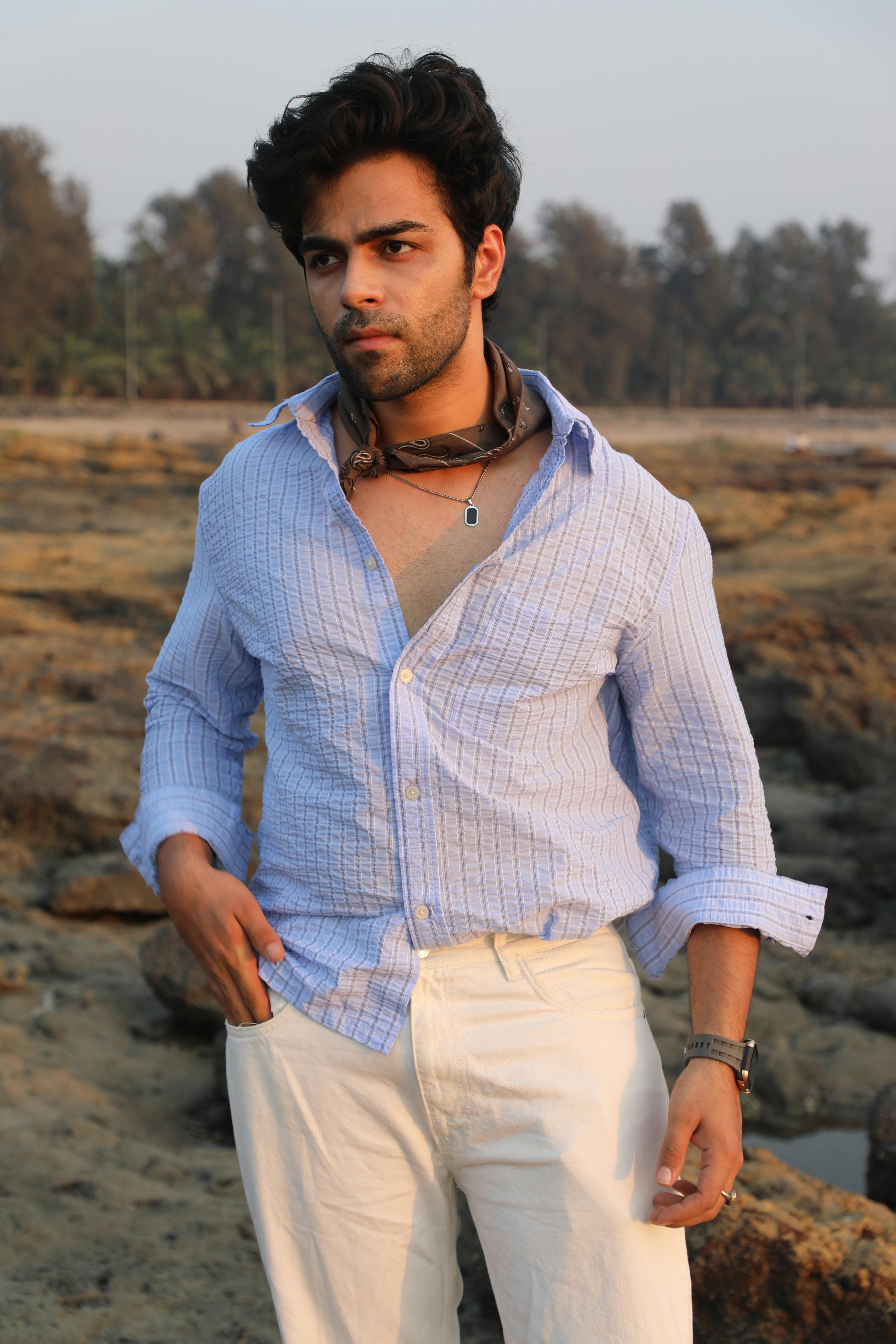 A man in casual attire stands confidently on a rocky beach at sunset.