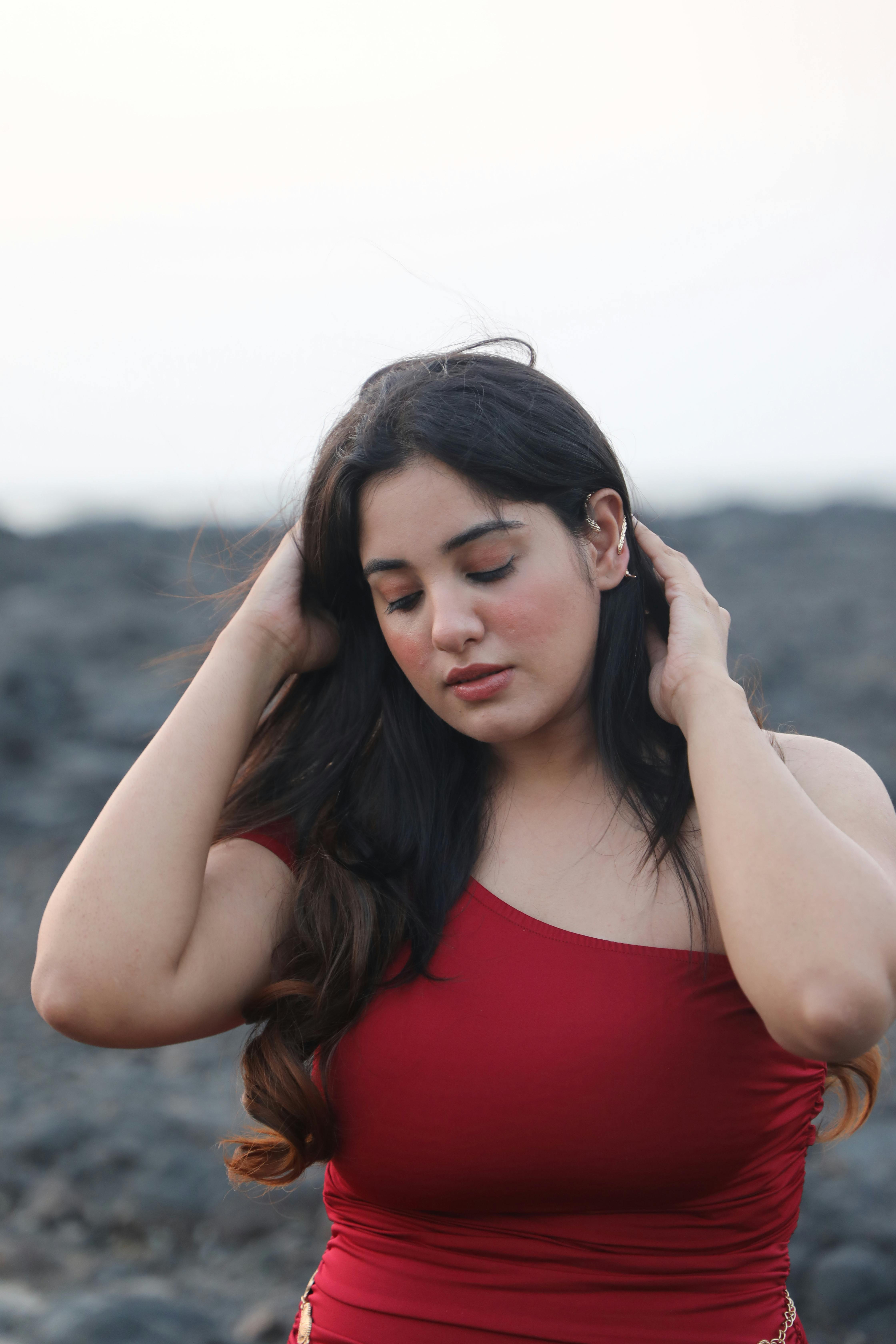 Woman in red dress with hands in hair against rocky outdoor backdrop.