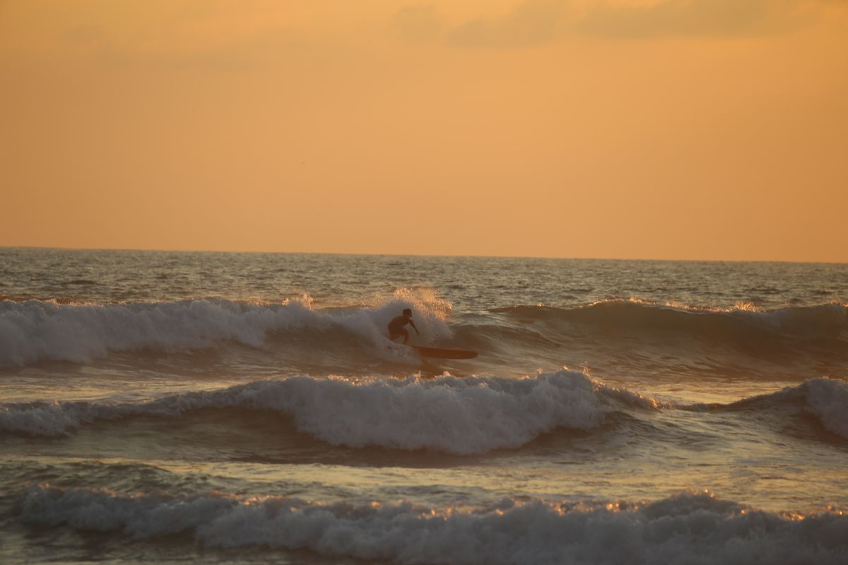Surfista montando olas al atardecer en México, con luz dorada sobre el océano