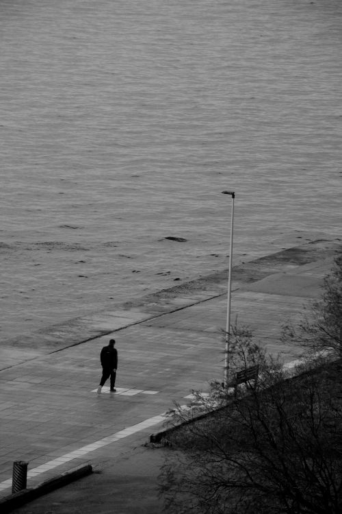 Free Solitary person strolling beside a vast empty seashore on a cloudy day. Stock Photo