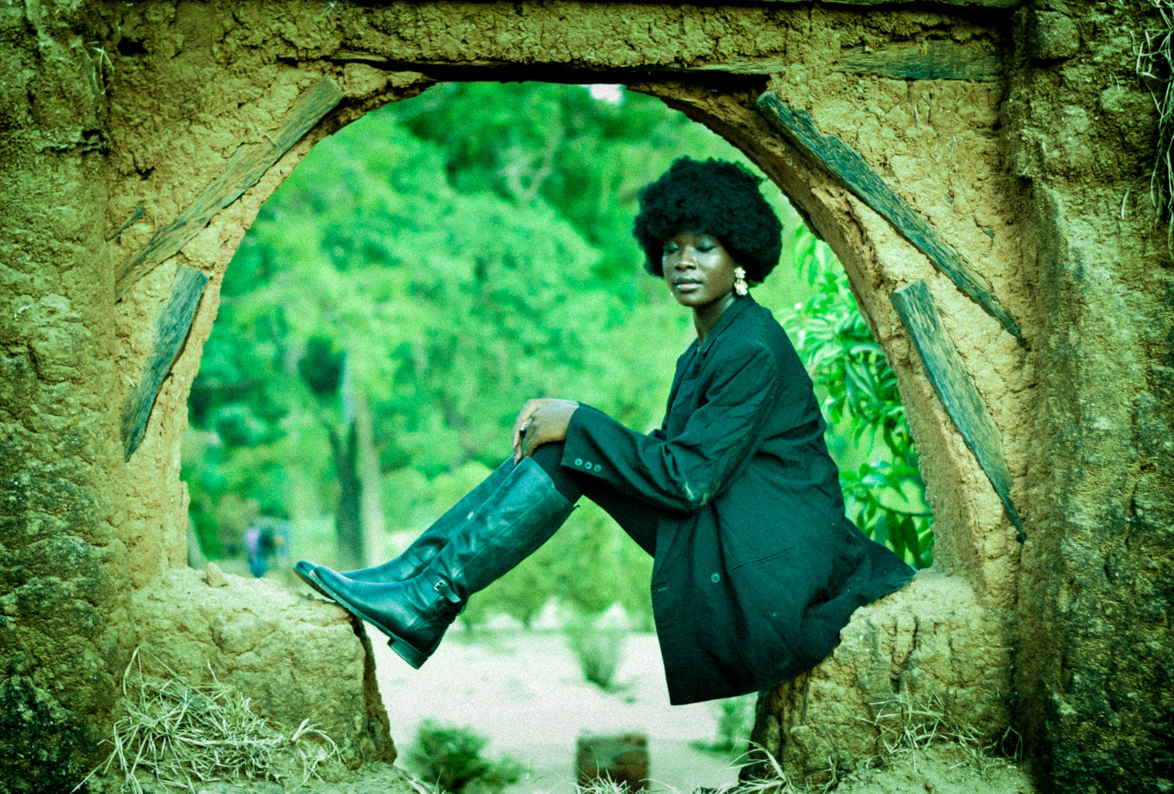 bezplatná Módní žena pózuje v rustikálním oblouku v černém oblečení a botách a vyzařuje eleganci a sebevědomí. Základová fotografie