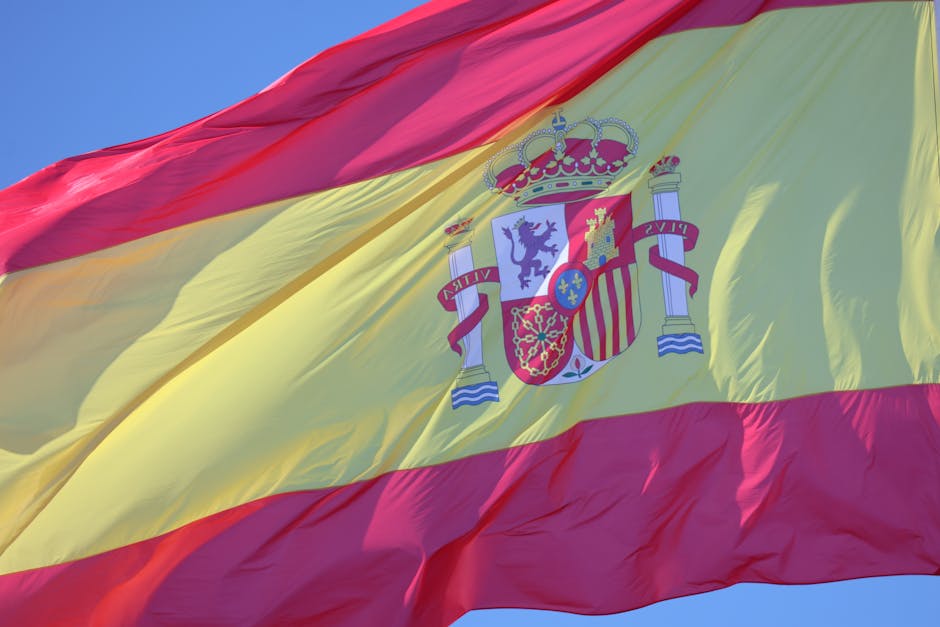 Close-up of the Spanish flag with its national insignia waving under a clear blue sky.