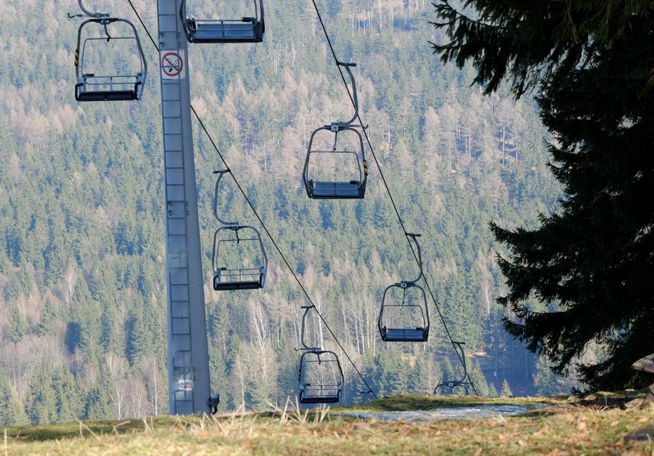 An empty ski lift in a serene mountain setting with lush green forest views.