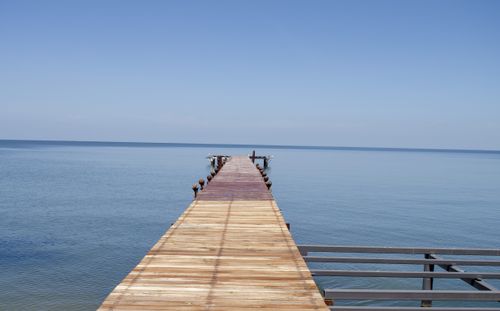 Free A tranquil wooden pier stretches into a calm, blue sea under a clear sky, perfect for serene travel imagery. Stock Photo