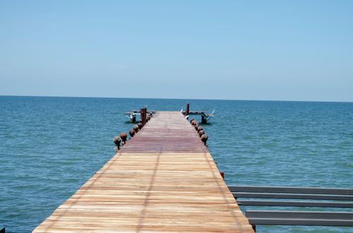 Free A tranquil scene of a wooden pier extending into a calm blue sea under a clear sky, perfect for escape and relaxation. Stock Photo