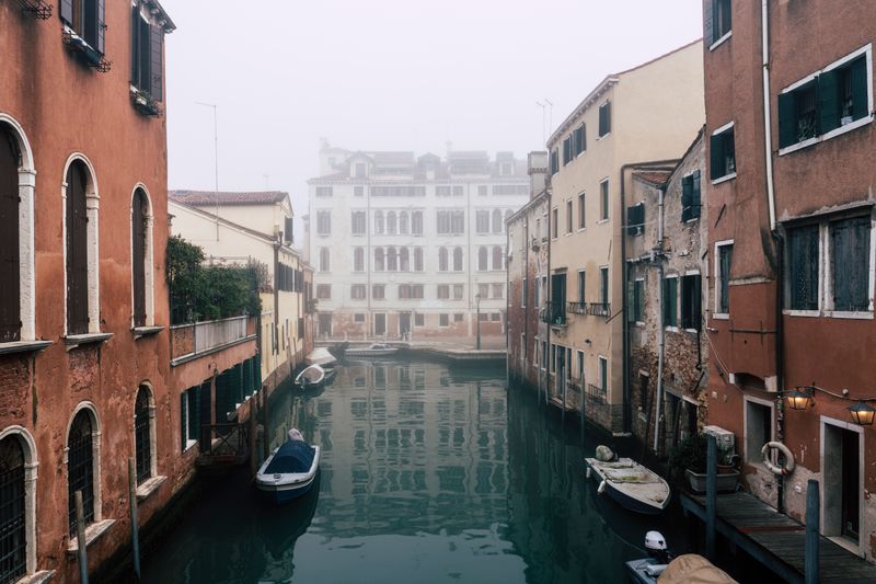 Canal venețian în ceață, între clădiri istorice, în lumina dimineții