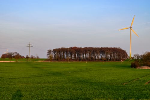Free A picturesque view of a wind turbine in green fields with trees and power lines in Coesfeld, Germany. Stock Photo