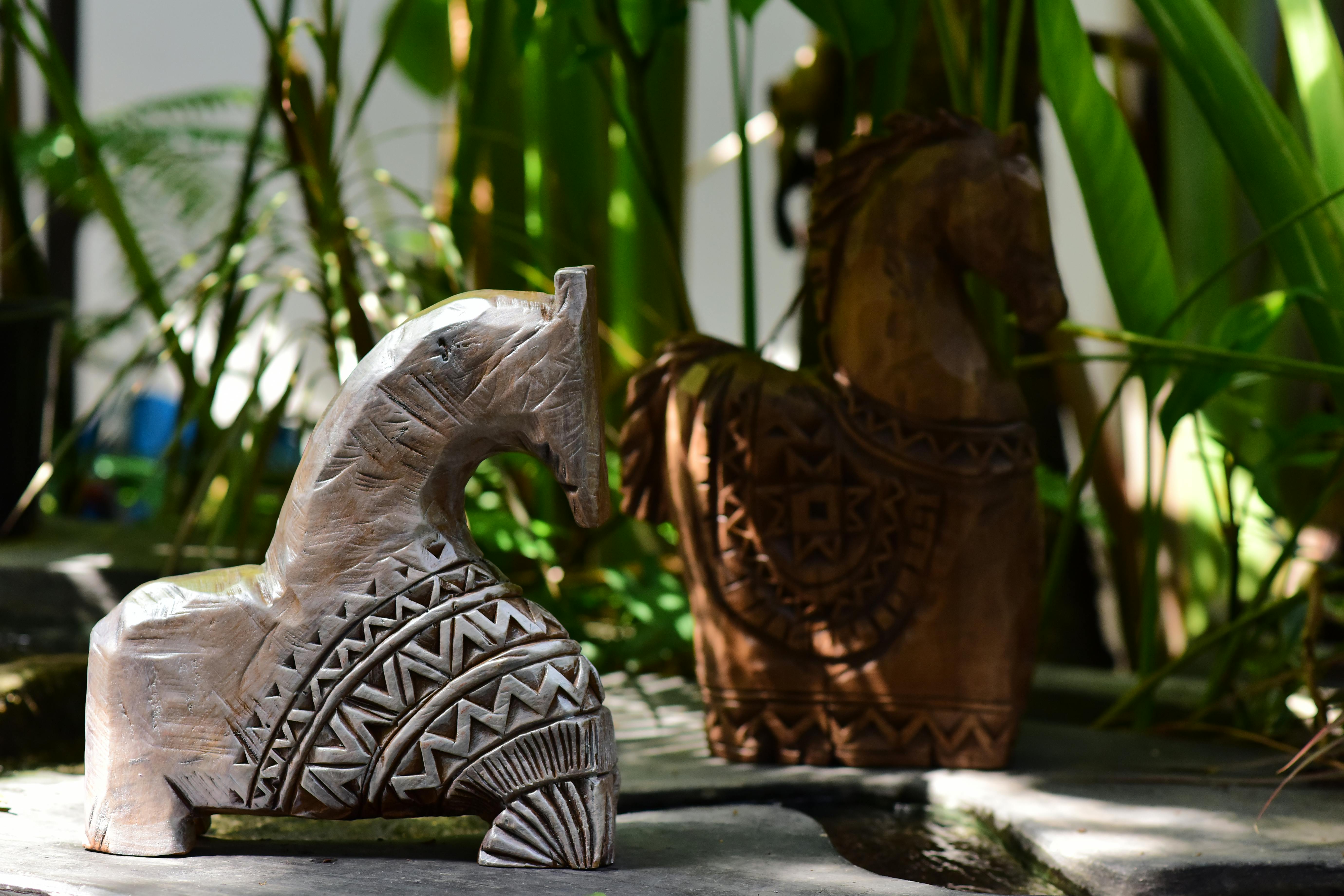 Zadarmo Dve zložito vyrezávané drevené sochy koní uprostred zeleného lístia, ktoré prezentujú remeselné spracovanie a prírodu. Fotka z fotobanky