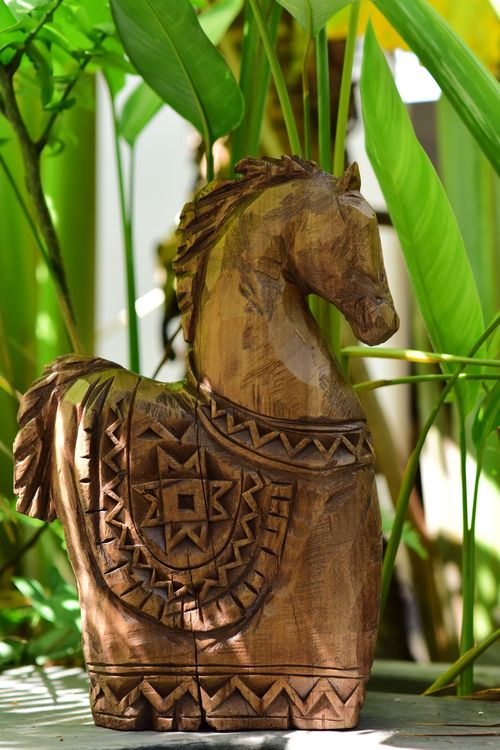 Free Intricately carved wooden horse statue surrounded by vibrant green foliage. Stock Photo