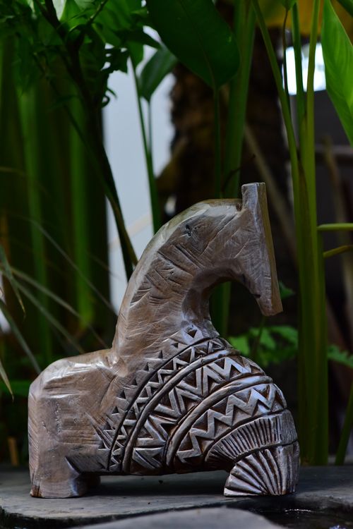 Free An elegantly carved wooden horse statue with tribal patterns set in a lush natural environment. Stock Photo