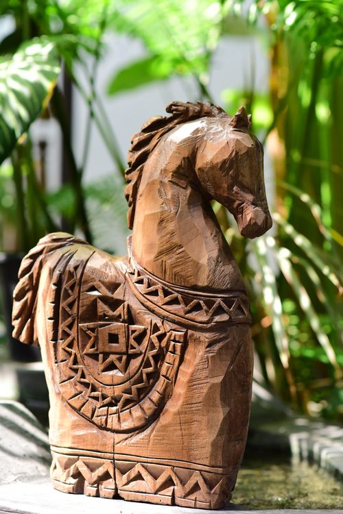 Free Beautifully carved wooden horse sculpture set against a lush garden backdrop. Stock Photo