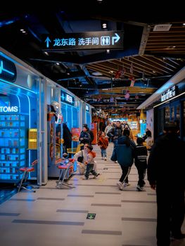 A vibrant shopping mall corridor with neon lights and busy shoppers, featuring signs in Chinese script.