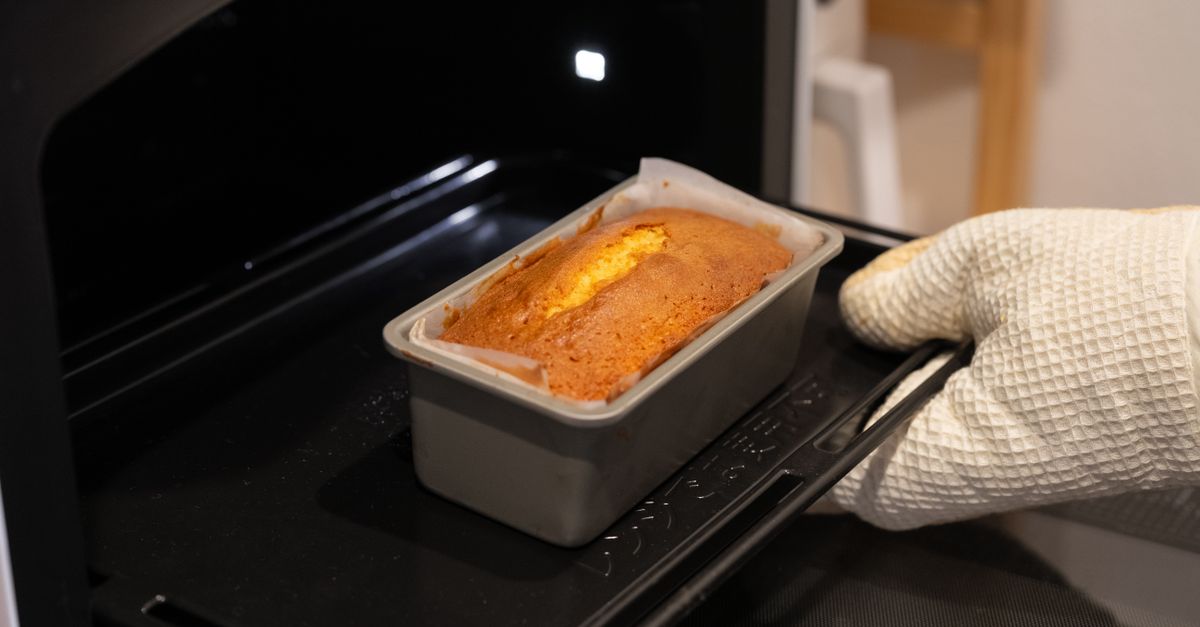 Um bolo sendo retirado de um forno usando uma luva branca, capturando o calor do preparo caseiro.