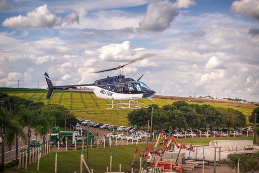 A helicopter gliding over lush fields with a vibrant blue sky backdrop.