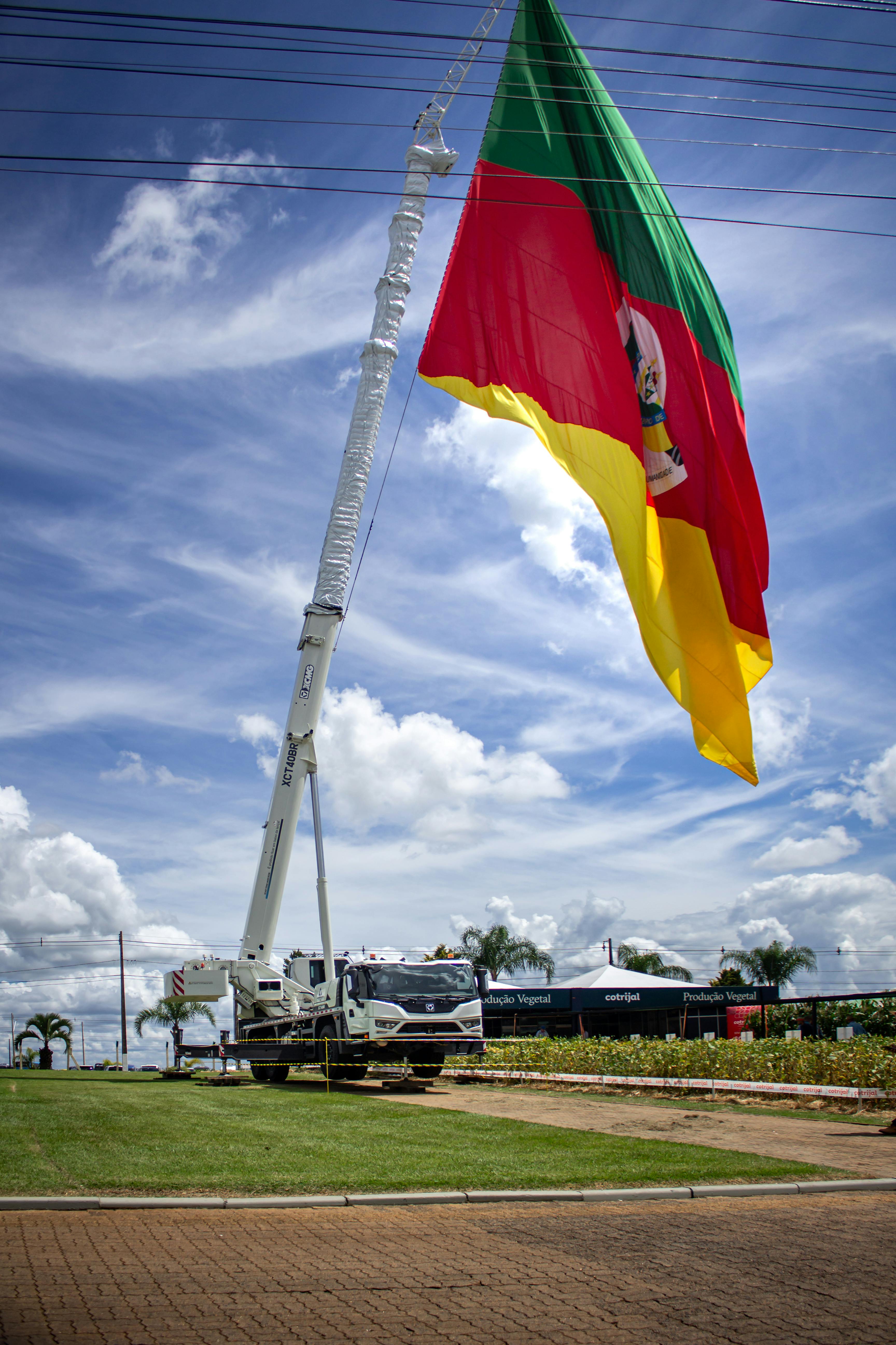 免費 一面鮮豔的旗幟由起重機升起，映襯著湛藍的天空，展現出一幅生氣勃勃的戶外景象。 圖庫相片