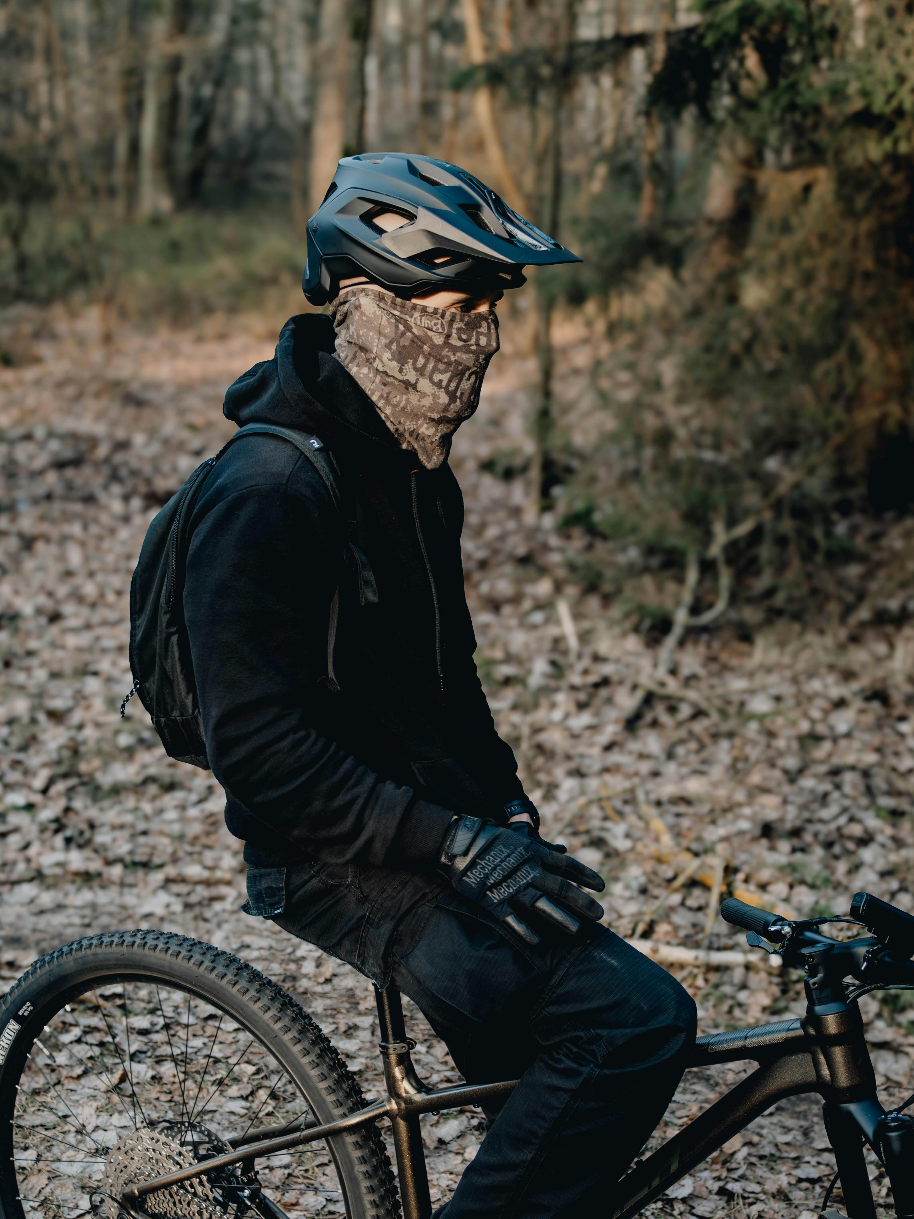 ฟรี นักปั่นจักรยานเสือภูเขาสวมหมวกกันน็อคและหน้ากาก ขี่ผ่านป่าในฤดูใบไม้ร่วง คลังภาพถ่าย