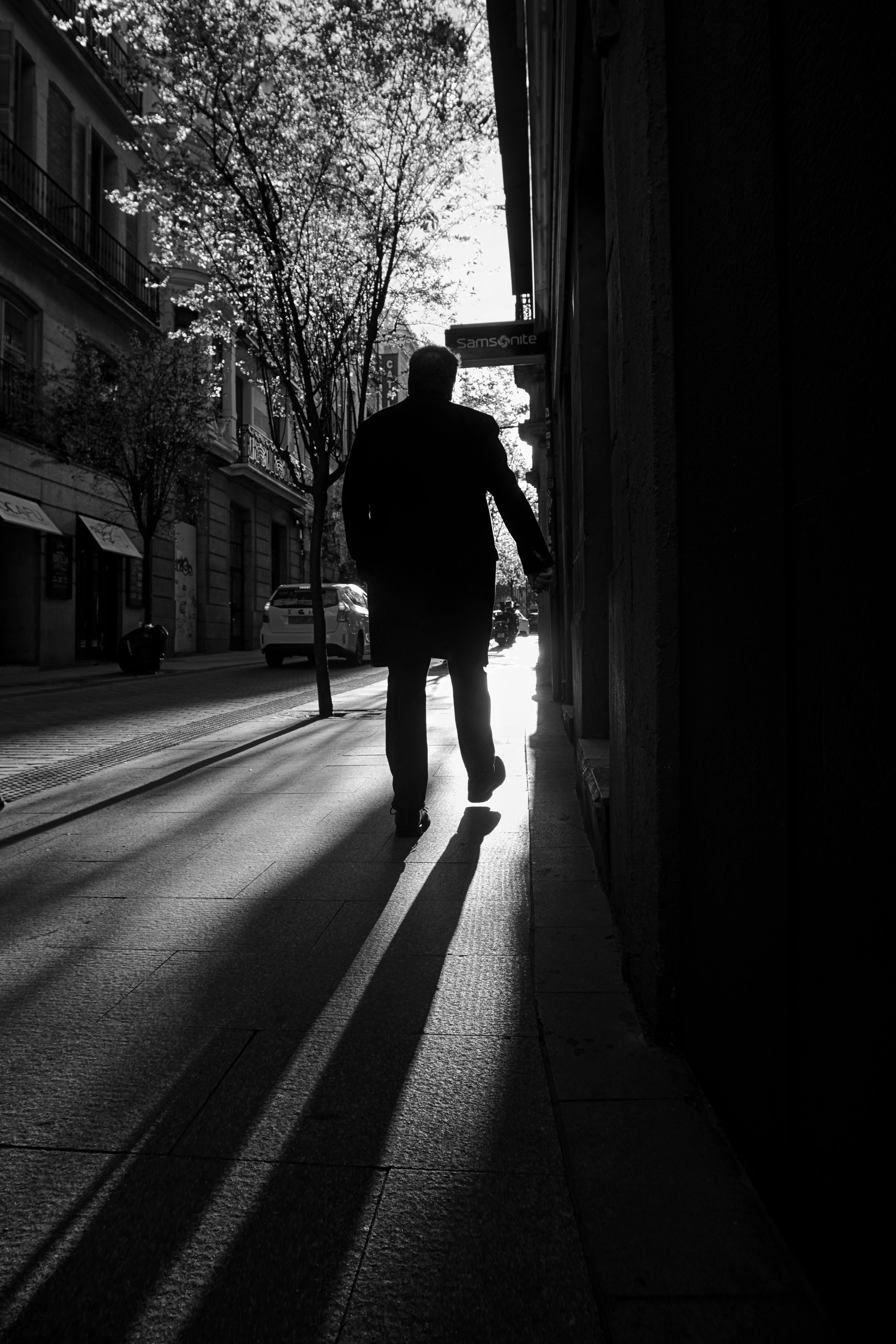 Безкоштовне Чоловік у силуеті йде затіненою міською вулицею Мадрида вдень, зафіксований у драматичному освітленні. стокове фото