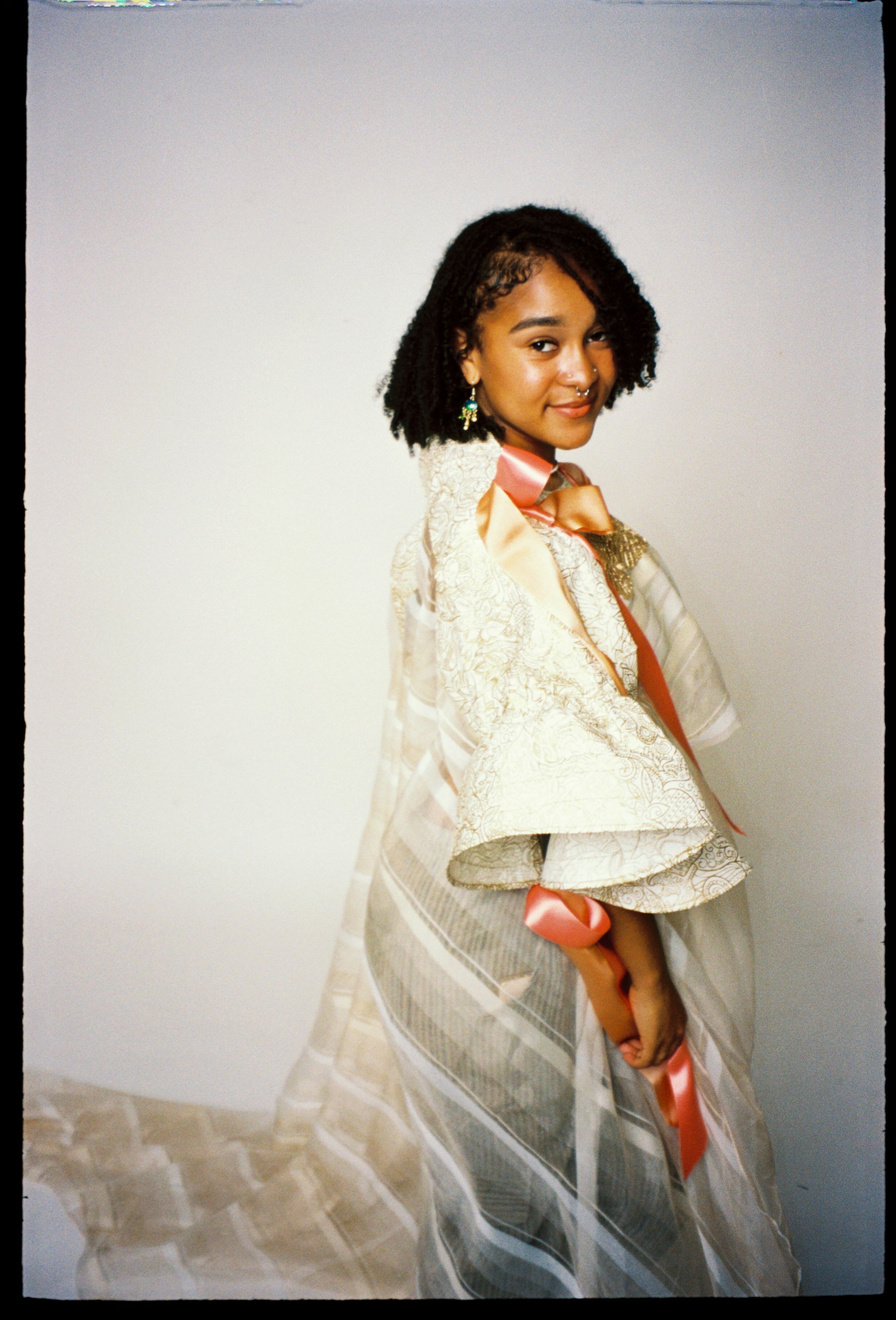 A young girl posing in an elegant dress with ribbons and lace, exuding charm and confidence.
